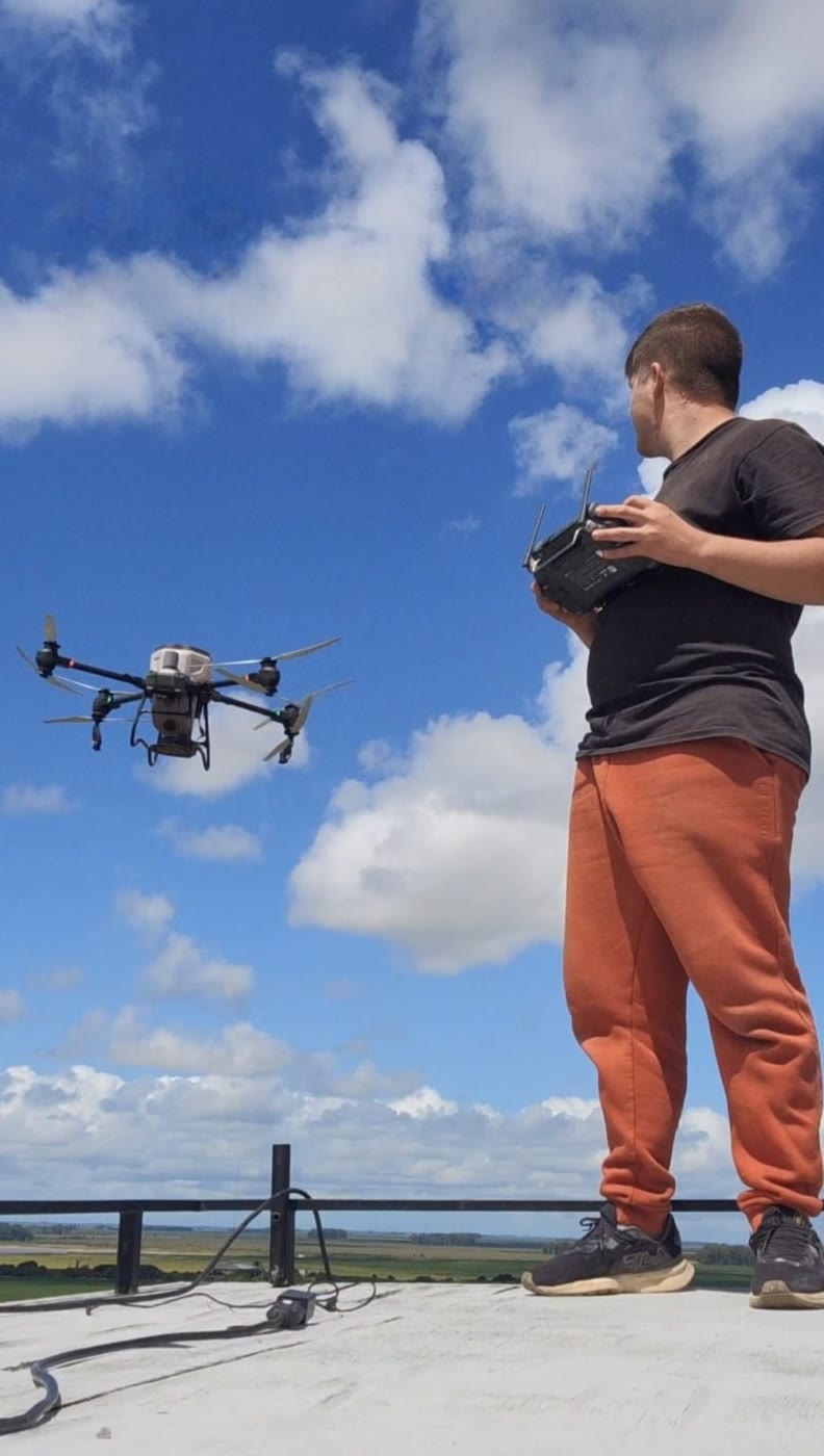Johann de pé num terraço, pilotando um drone agrícola contra o céu azul.