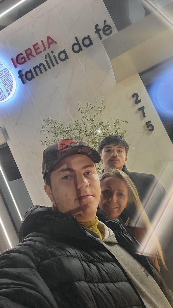 Selfie de Johann com mais duas pessoas na entrada da Igreja Família da Fé.